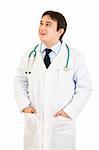 Smiling doctor with hands in pockets looking up at copy space isolated on white