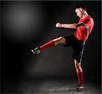 handsome soccer player kicks ball on black background