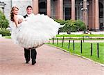 groom is carrying bride on arms on city park road