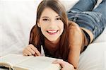 Beautiful woman reading a book, lying on a sofa in a living-room