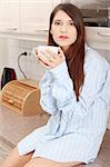 A young woman having morning coffee or tea in the kitchen