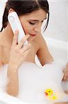 Beautiful young woman talking by wireless phone while taking a bath