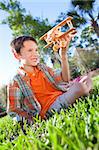 A young boy outside sitting on the grass playing with his model airplane