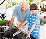 Father shows his son how to put a clean air filter in the car engine.