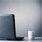laptop and cup of hot evaporating coffee on table, blue toned