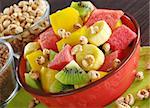 Fresh fruit salad made of banana, kiwi, watermelon and mango pieces in orange bowl with cereals (puffed wheat and puffed chocolate quinoa) (Selective Focus, Focus on the front of the bowl and the fruits in the front)