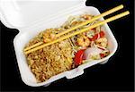 Chinese takeout food: Fried rice with king prawns and vegetables with wooden chopsticks in a styrofoam box photographed from top on black