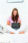 Concentrated pretty woman sitting on sofa at home and using laptop