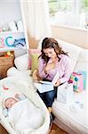 Bright woman sitting on the sofa with bags reading a card while her baby is sleeping in his cradle at home