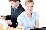 Couple of bright businesspeople using laptop and reading newspaper during breakfast against a white background