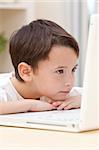 A young boy child resting on his hands and looking at the screen while using laptop computer