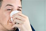 Close-up of a man holding a  tissue on his nose.