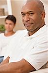 A happy African American man and woman couple in their thirties sitting at home, the man is in focus in the foreground the woman out of focus in the background.