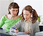 Teenager girl sitting together with her mother and showing her homework