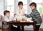 Three twin brothers playing chess game in room