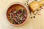 Black, red, green and white peppercorns in wooden mortar with pestle on wooden board photographed from above (Selective Focus, Focus on the peppercorns in the mortar)