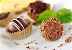 Chocolate truffles with mint leaf, fine chocolate shavings and a yellow cake in the background (Very Shallow Depth of Field, Focus on the front of the first praline)