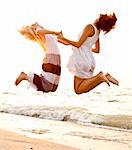 Two beautiful young girlfriends jumping on the beach at sunset. Photo with counter-light on background.