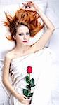 Fashion red-haired girl with rose in the bedroom. Studio shot from top.