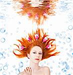 Beautiful red-haired girl with tulips in hair underwater. Art photo.