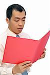 Surprised business man reading paper in red folder of document, half length closeup portrait on white background.