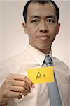 Mature executive of Asian holding A plus card in yellow, half length closeup portrait.
