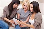 Three beautiful young women friends at home using tablet computer and laughing