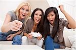 Three beautiful interracial young women friends at home having fun playing computer games together and laughing