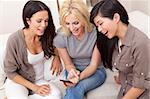 Three beautiful young women friends at home using a smartphone and laughing