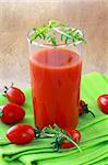 glass of tomato juice on the green cloth, with a cherry tomato