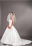 beautiful bride is standing in wedding dress on grey background, side view