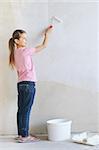 Girl painting a wall with roller .