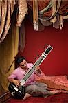 Young India man plays a sitar under ornate curtains