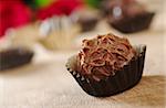 Closeup of a milk chocolate truffle with wrapping, with other truffles and red roses in the background photographed on wood (Very Shallow Depth of Field, Focus on the front of the first praline)