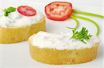 Baguette bread with cream cheese spread decorated with tomato, parsley and green onion on white plate (selective focus)