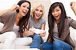 Three beautiful interracial young women friends at home having fun playing video games together and laughing