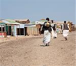 Three local egyptian men walking up dirt road in a rural african settlement