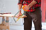 A detail of a man cutting wood with a small hand saw