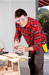 A man wearing saftey goggles using an electric hand sander