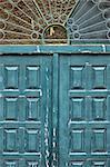 Weathered blue wooden gate with vintage ornamental sun pattern metalwork.