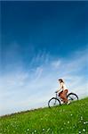 Happy young woman on a green meadow riding a bicycle