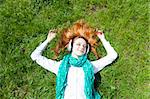Redhead girl with headphone lies in the park.