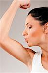 sporty woman is kissing her biceps muscle on grey background