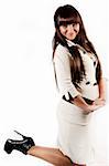 A young girl with long dark hair stands sideways to the camera. One of her legs bent at the knee. White background.