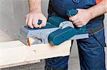Close-up of a construction worker's hand and power tool while planing a piece of wood trim for a project.