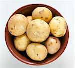Fresh potatoes unpeeled potatoes in clay bowl, top view. Light background