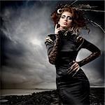 High fashion model in black dress, with long nails and creative hairstyling and makeup in stormy weather