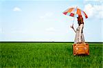 Redhead enchantress with umbrella and suitcase in a spring wheat field.