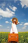 Redhead enchantress with suitcase at spring rapeseed field.