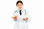 Smiling medical doctor with pills in one hand and apple in other isolated on white